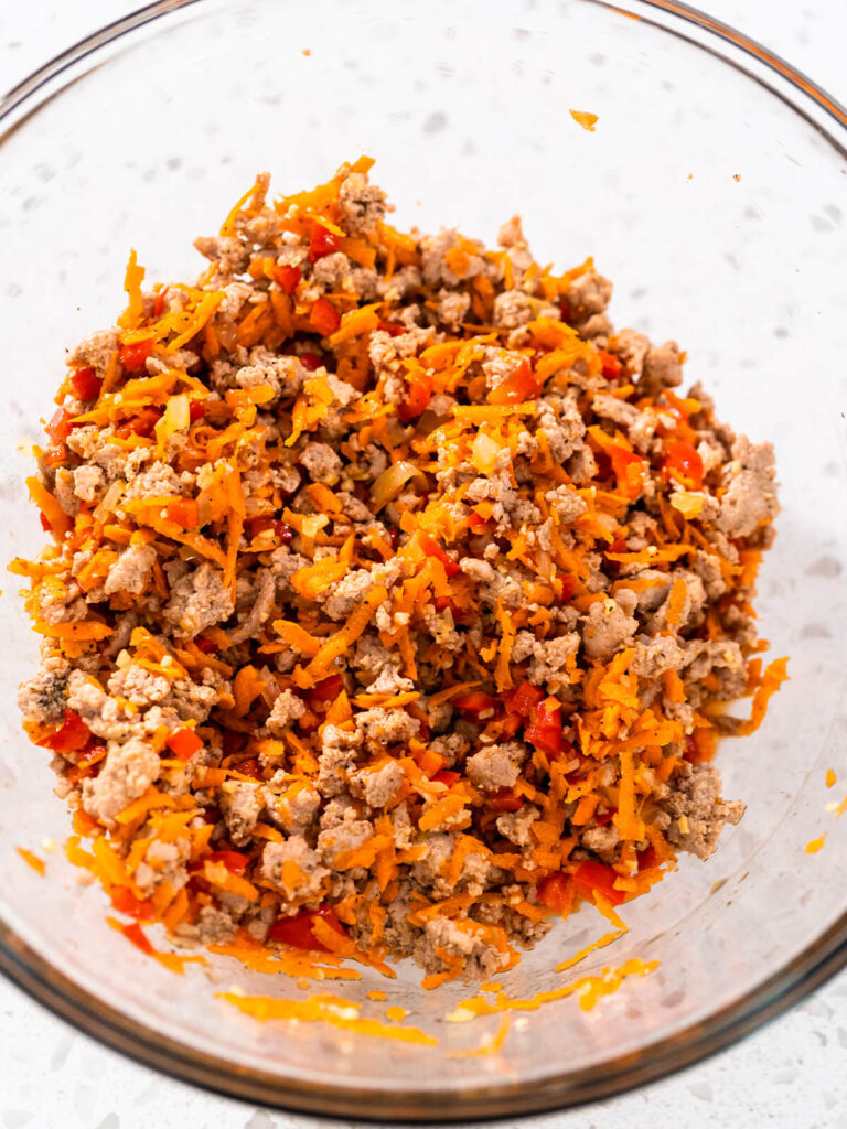 Fertige Füllung aus Putenhackfleisch, grob geriebenen Karotten und roter Paprika in einer Glasschüssel