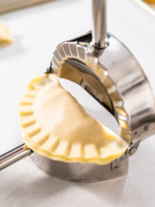 Geformte Empanada mit geriffeltem Rand in der halb geöffneten Teigtaschenpresse