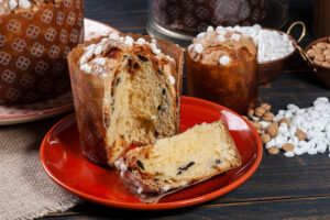 Angeschnittener Schoko-Panettone auf rotem Teller, davor eine Scheibe mit dunklen Schokoladenstücken und Hagelzucker