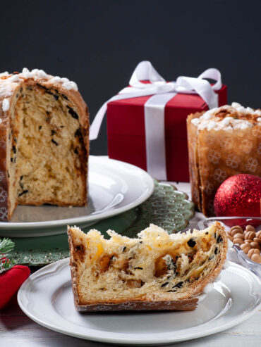 Aufgeschnittener Panettone in der Papierform mit heller Krume und dunklen Schokoladenstücken, davor eine Scheibe mit Hagelzucker auf dem Rand
