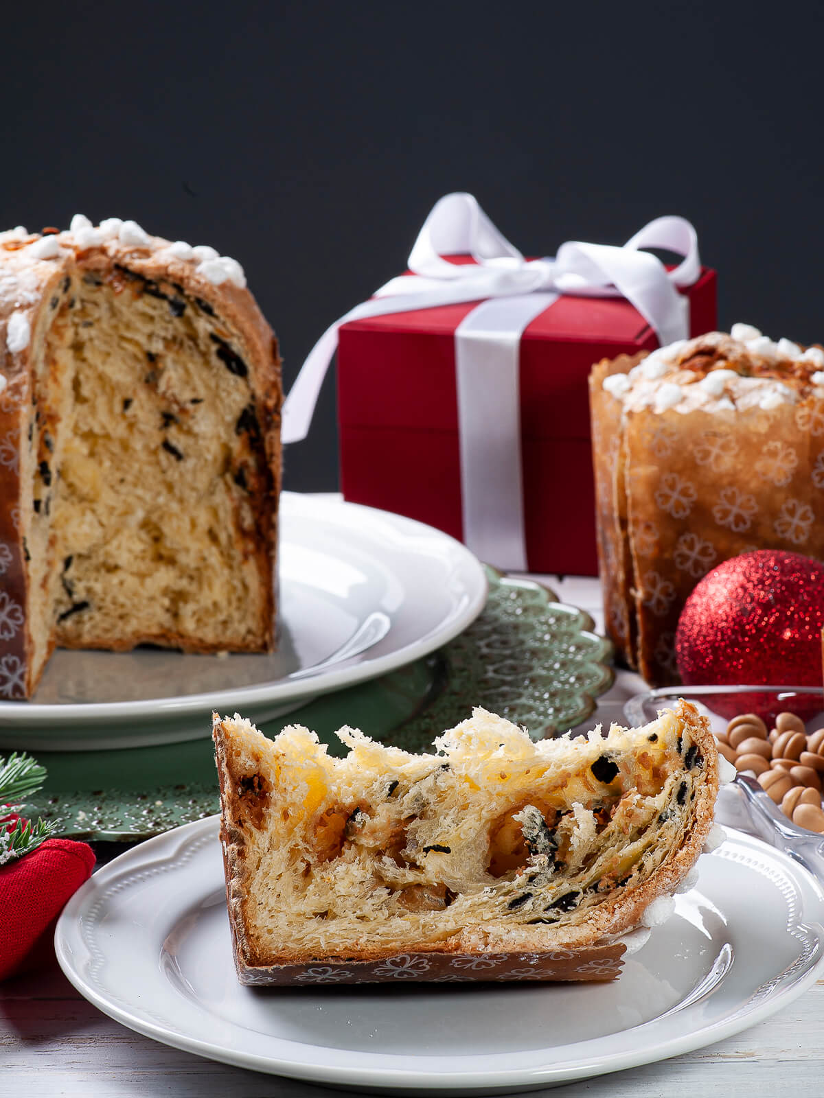 Aufgeschnittener Panettone in der Papierform mit heller Krume und dunklen Schokoladenstücken, davor eine Scheibe mit Hagelzucker auf dem Rand