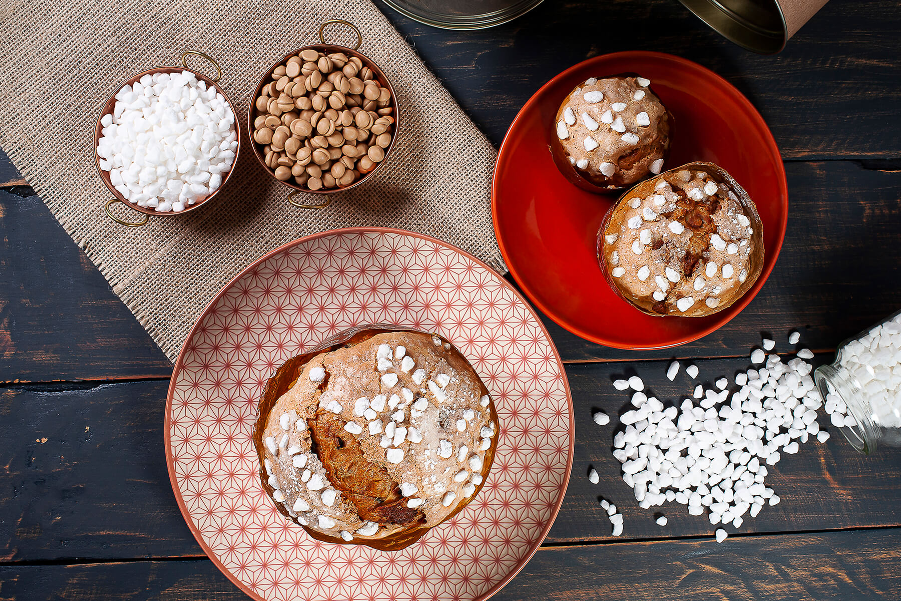 Drei Panettone von oben mit Hagelzucker auf der Kuppe, daneben Schälchen mit grobem Zucker und hellbraunen Schokoladentropfen