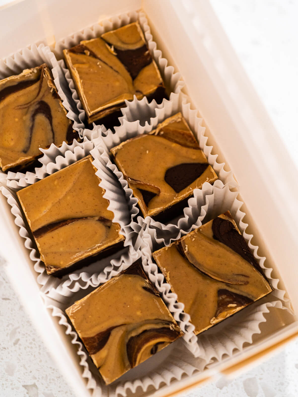 Fudge-Würfel in Papierförmchen in einer flachen weißen Geschenkschachtel