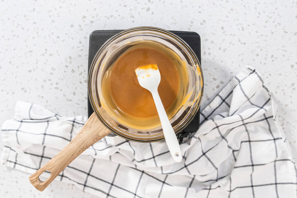 Geschmolzene Erdnussbutter-Creme mit weißer Schokolade in einem Glastopf auf der Kochplatte