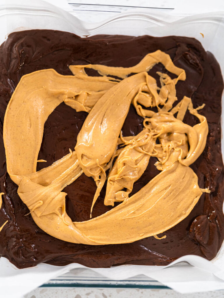 Breite Streifen heller Erdnussbutter-Creme auf der dunklen Fudge-Masse in der Backform
