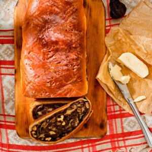 Schweizer Birnbrot mit dunkler Dörrbirnen-Füllung auf einem Holzbrett, daneben eine angeschnittene Scheibe und Butter