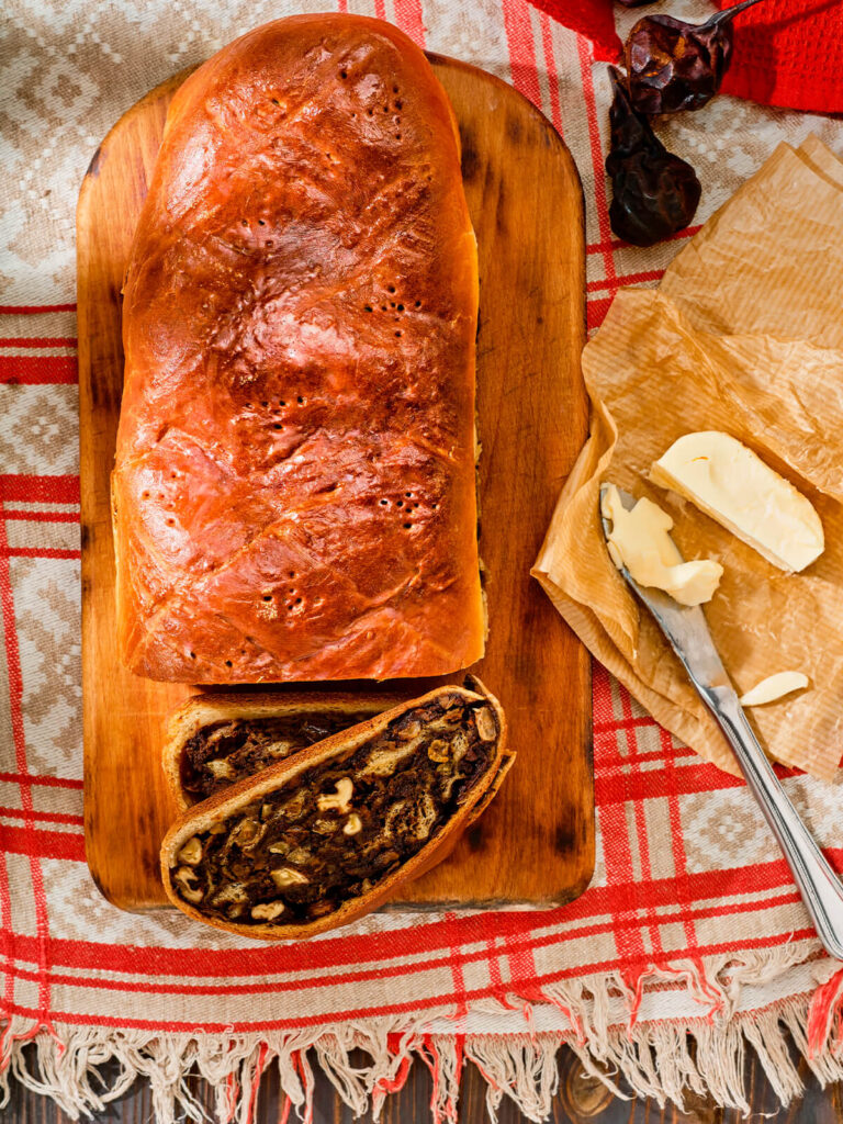 Schweizer Birnbrot mit dunkler Dörrbirnen-Füllung auf einem Holzbrett, daneben eine angeschnittene Scheibe und Butter