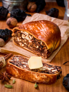 Angeschnittener Birnbrot-Laib und eine dicke Scheibe mit Butter, dahinter Zimtstangen und Sternanis