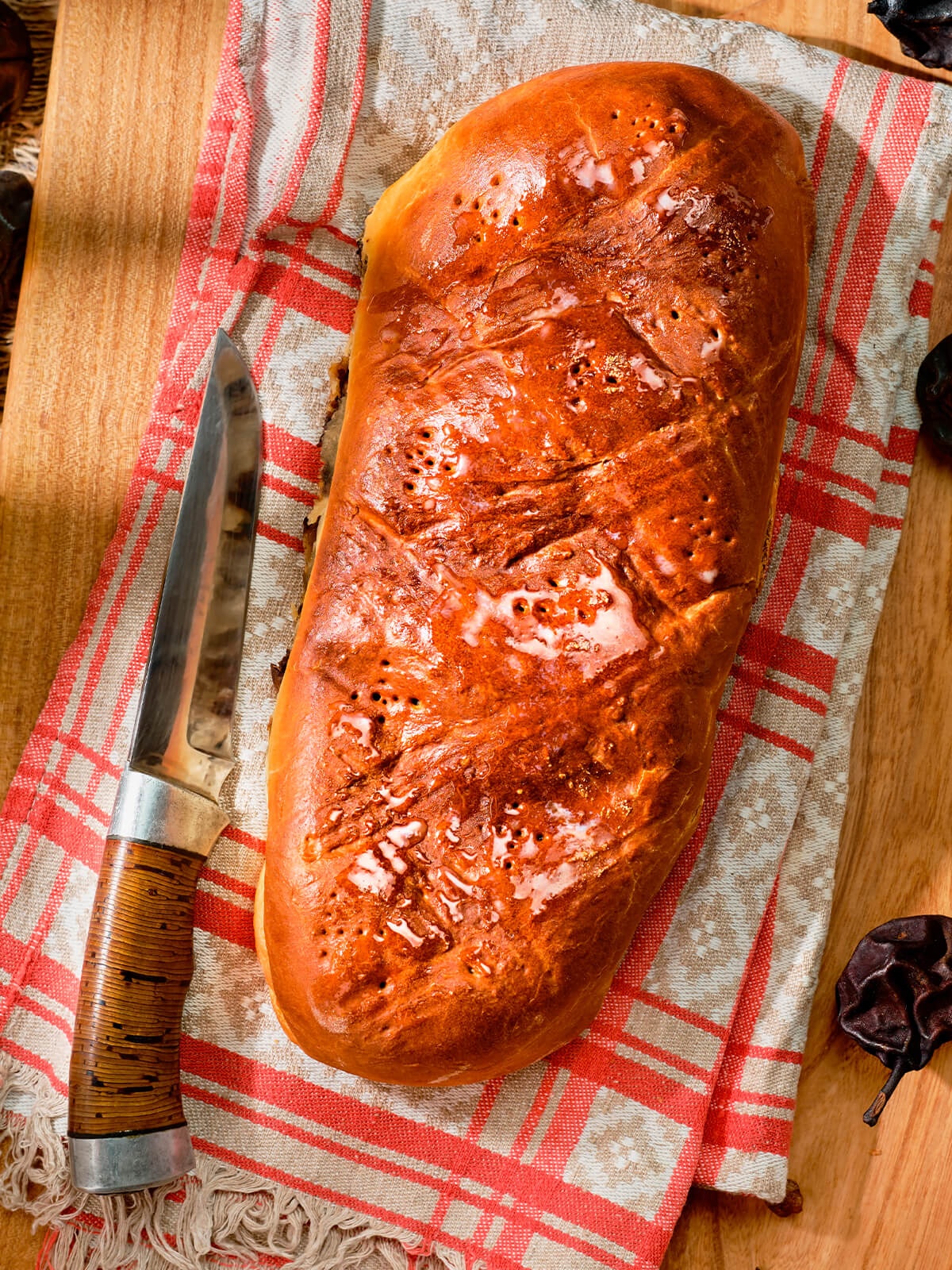 Ganzer Schweizer Birnbrot-Laib mit glänzender Kruste und eingestochenen Löchern auf einem rot-weiß karierten Tuch
