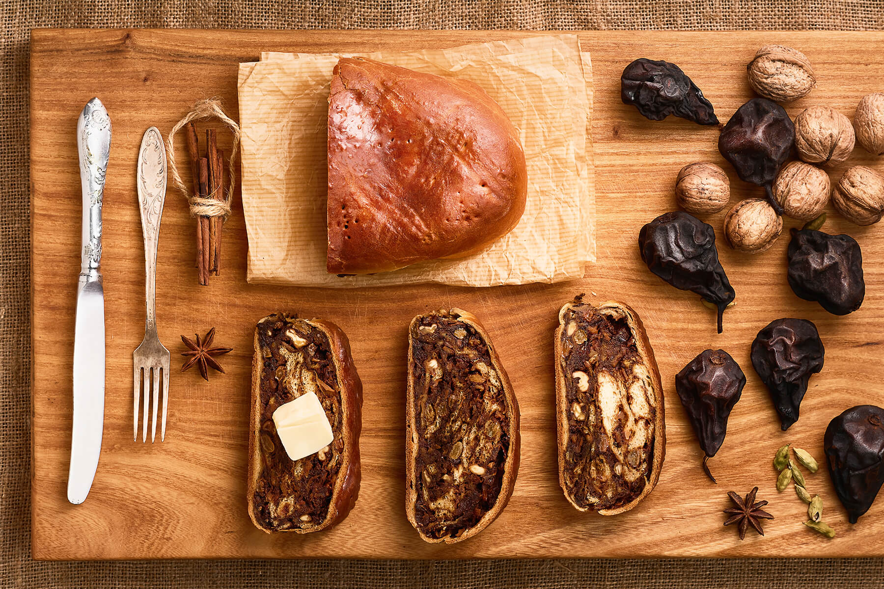 Aufgeschnittenes Schweizer Birnbrot mit Dörrbirnen-Walnuss-Füllung neben ganzen Dörrbirnen, Baumnüssen, Zimt, Sternanis und Kardamom