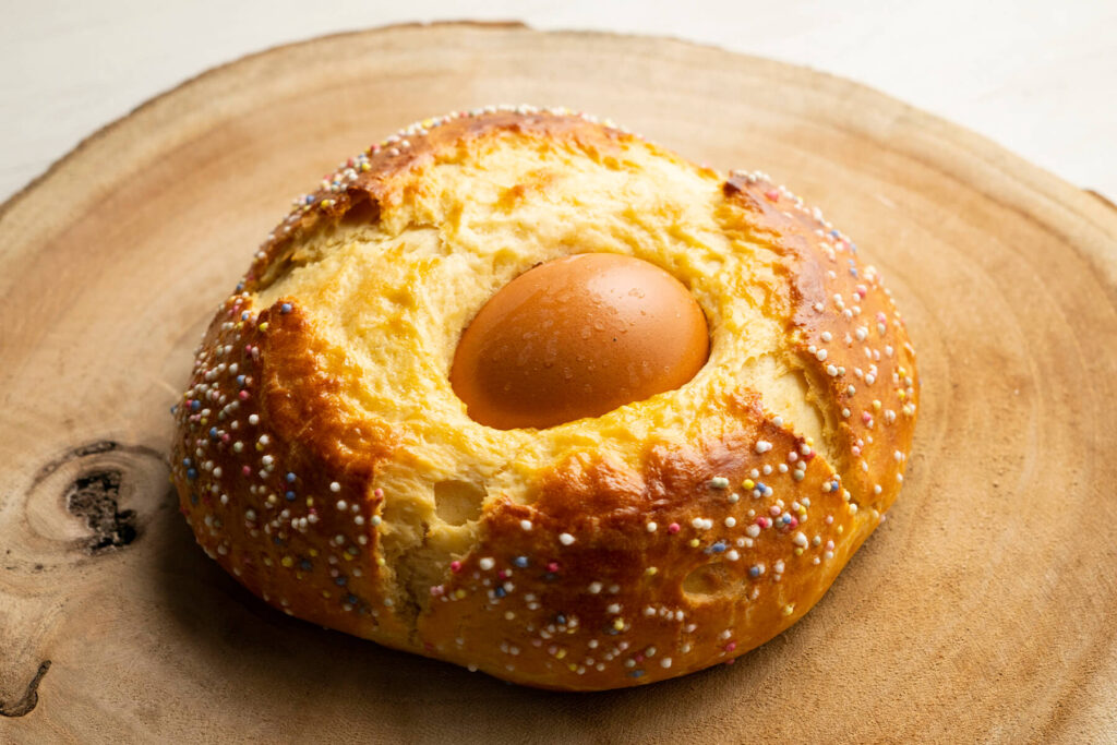 Spanisches Osterbrot Mona de Pascua mit eingebackenem braunem Ei und bunten Zuckerperlen auf einer Holzscheibe