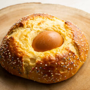 Spanisches Osterbrot Mona de Pascua mit eingebackenem braunem Ei und bunten Zuckerperlen auf einer Holzscheibe