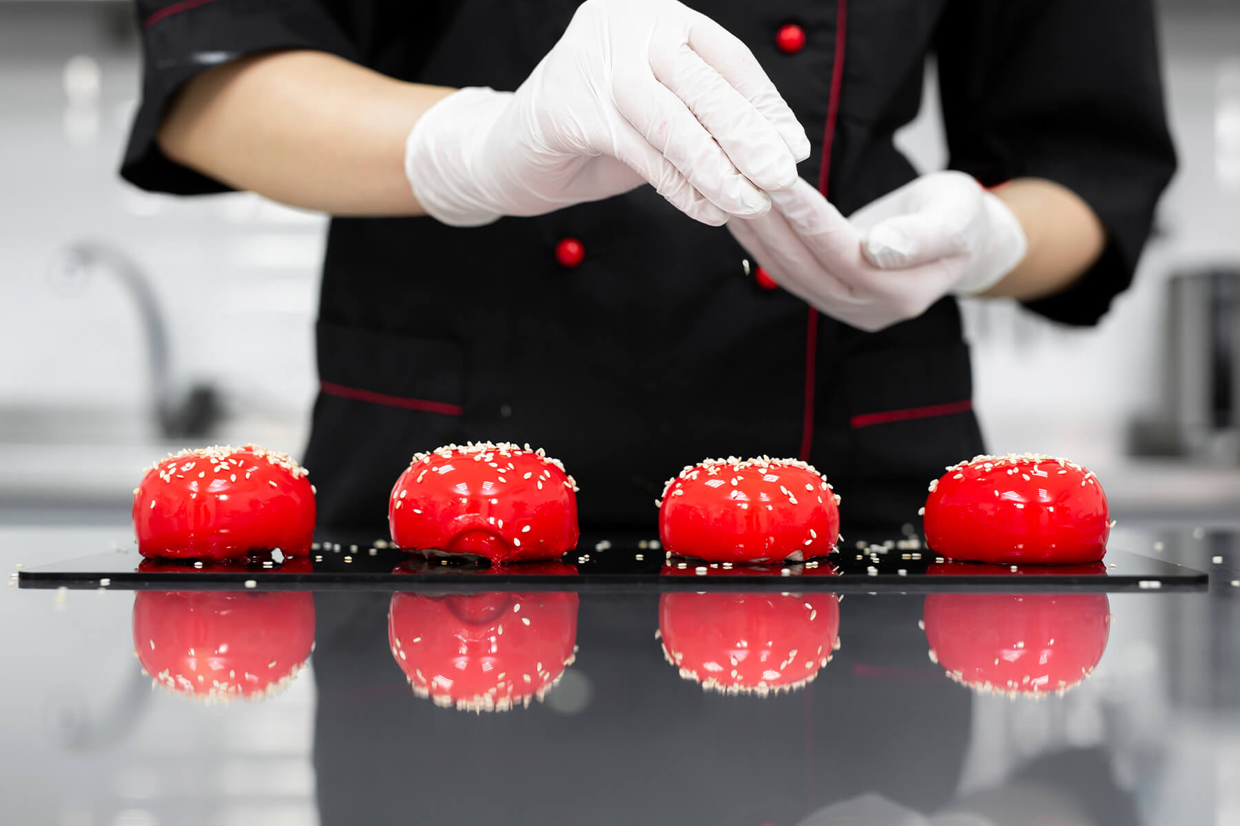 Vier glasierte Törtchen mit spiegelnder roter Oberfläche und Sesam auf einer schwarzen Platte