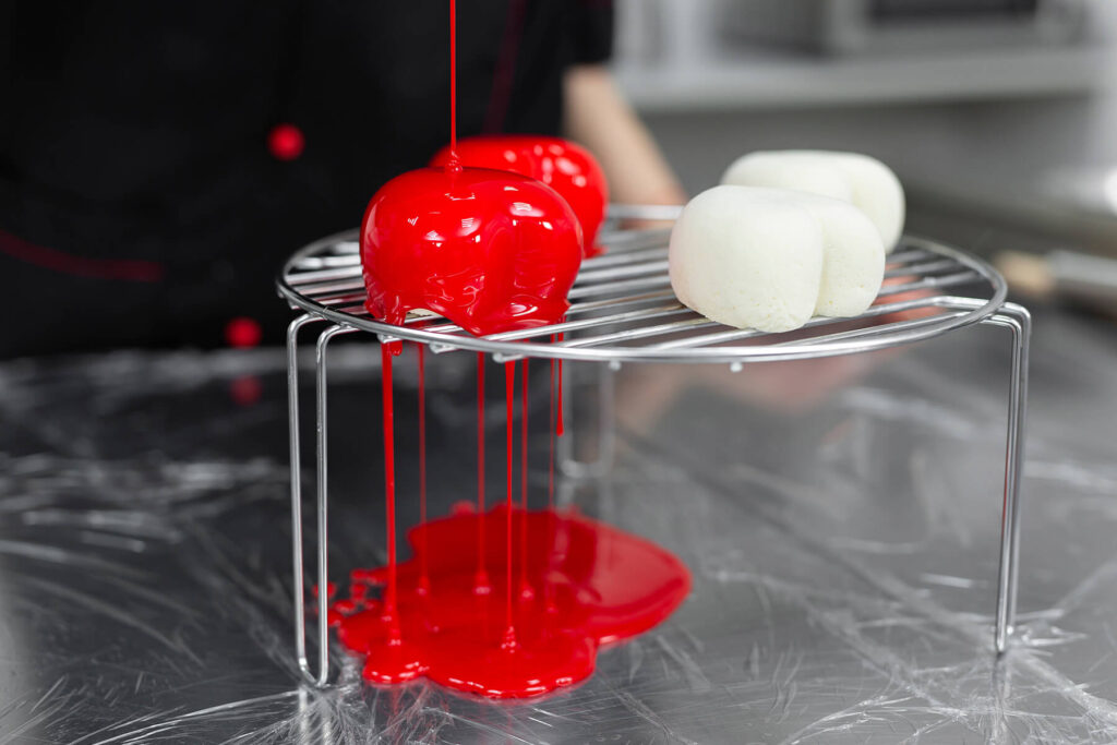 Rote Spiegelglasur wird über einen gefrorenen hellen Mousse-Rohling auf dem Kuchengitter gegossen