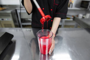 Fertig emulgierte rote Spiegelglasur läuft glänzend vom Stabmixer in den Becher zurück