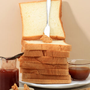 Hoher Stapel Toastbrotscheiben mit heller feinporiger Krume, oben eine aufrecht stehende Scheibe mit Erdnussbutter