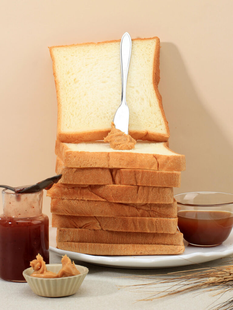 Hoher Stapel Toastbrotscheiben mit heller feinporiger Krume, oben eine aufrecht stehende Scheibe mit Erdnussbutter