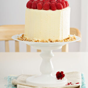Hohe vertikale Biskuittorte mit heller Frischkäsecreme, Himbeeren obenauf und Bröselkranz am Sockel