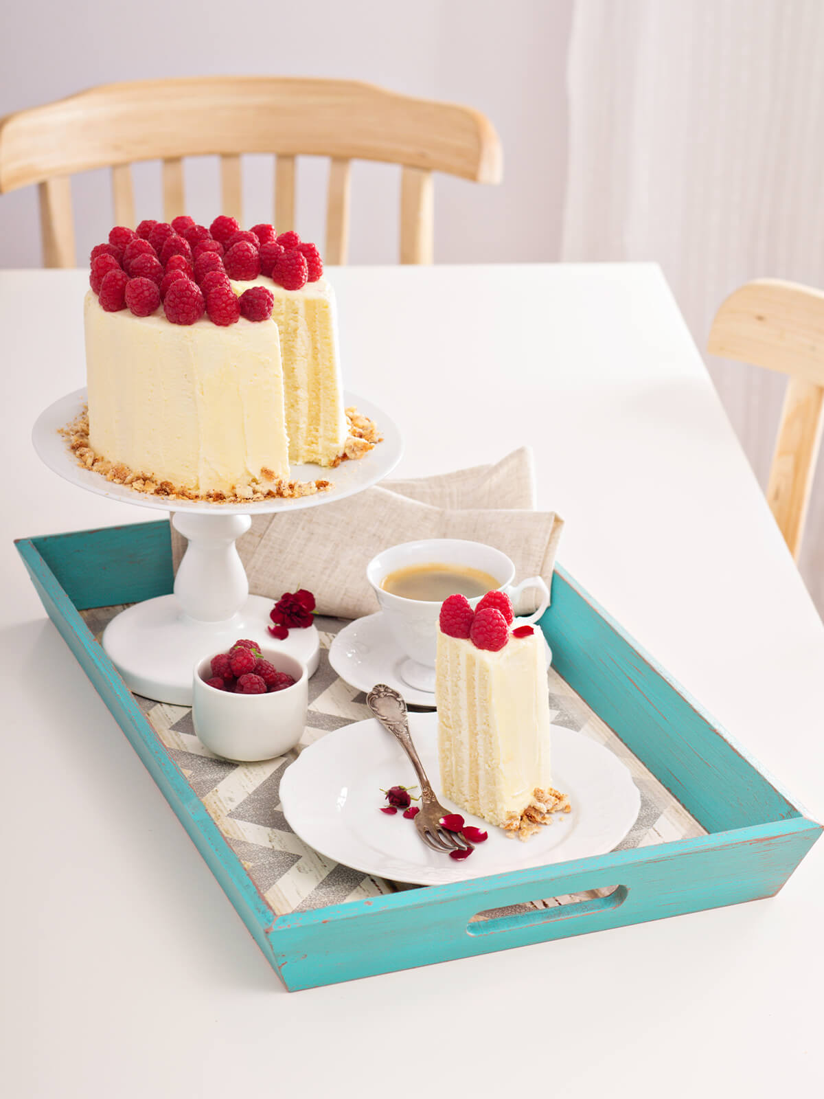 Vertikale Biskuittorte auf einer Etagere neben einem Stück auf dem Teller und einer Tasse Kaffee