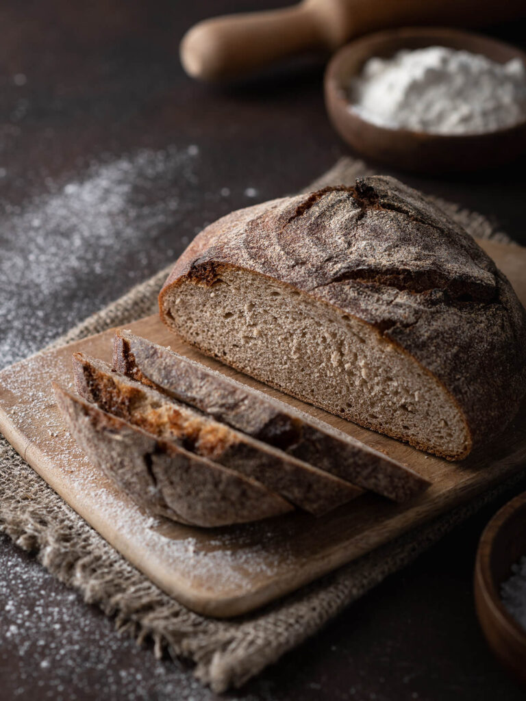 Angeschnittenes Vollkorn-Kartoffelbrot auf einem bemehlten Holzbrett mit heller feinporiger Krume