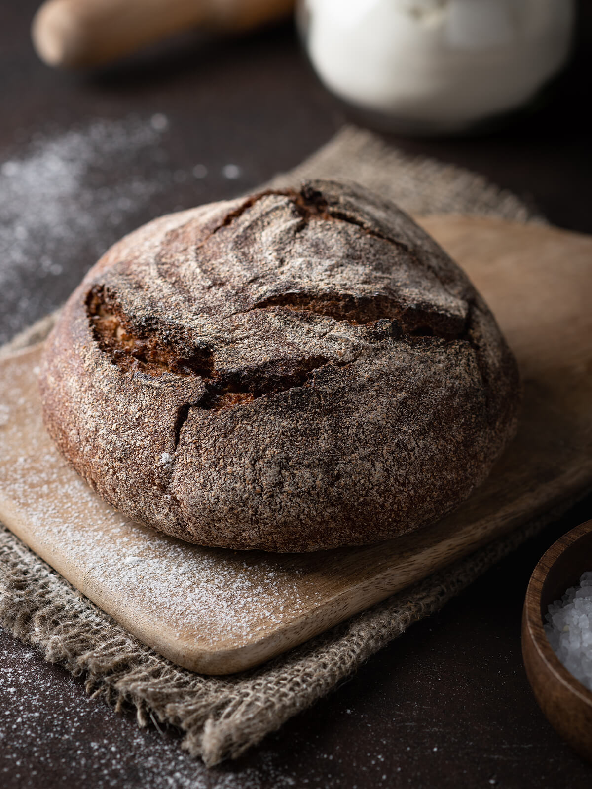 Runder Laib Vollkorn-Kartoffelbrot mit dunkler aufgerissener Kruste auf einem bemehlten Holzbrett