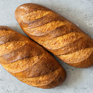 Zwei goldbraune Laibe Weißbrot aus Sauerteig-Resten mit je fünf Schrägschnitten