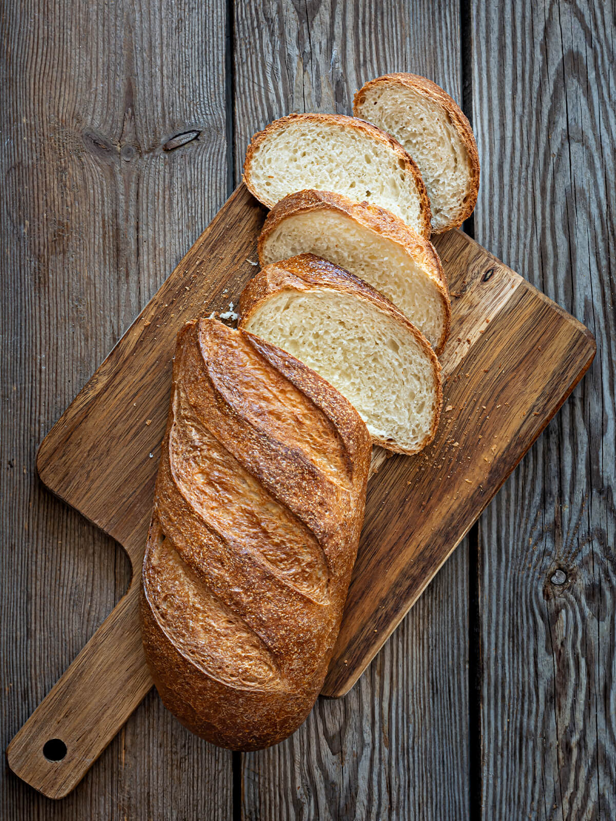 Aufgeschnittenes weiches Weißbrot aus Sauerteig-Resten mit fünf Schrägschnitten auf einem Holzbrett