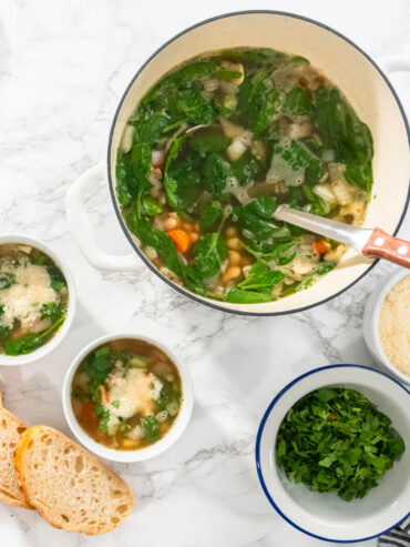 Weiße Bohnensuppe mit Spinat und Parmesan in kleinen Schalen neben dem Topf und geröstetem Weißbrot