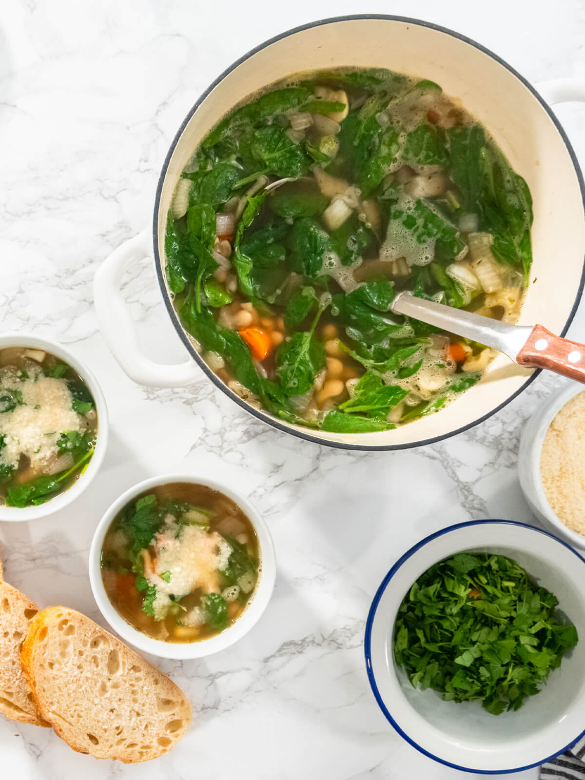 Weiße Bohnensuppe mit Spinat und Parmesan in kleinen Schalen neben dem Topf und geröstetem Weißbrot