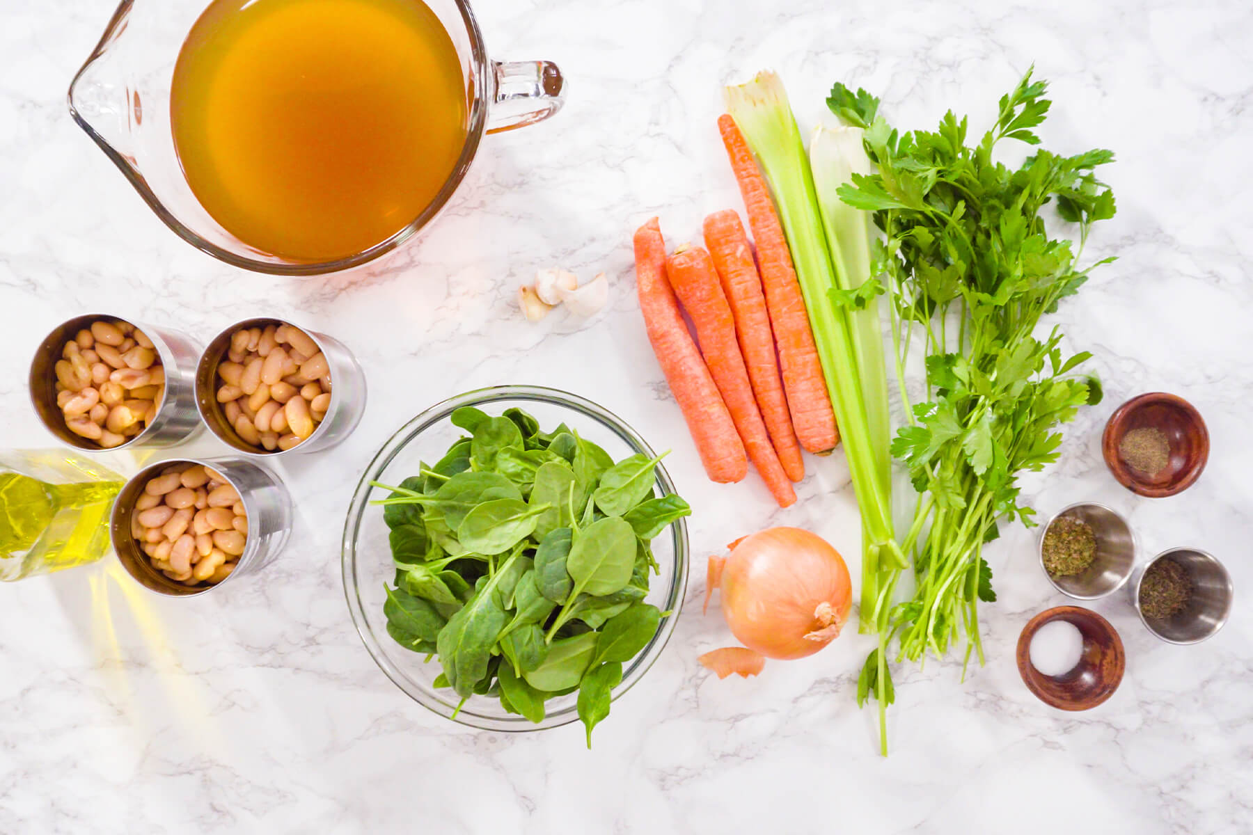 Zutaten für weiße Bohnensuppe: Gemüsebrühe, drei Dosen weiße Bohnen, Babyspinat, Karotten, Staudensellerie, Zwiebel, Knoblauch, Petersilie und getrocknete Kräuter