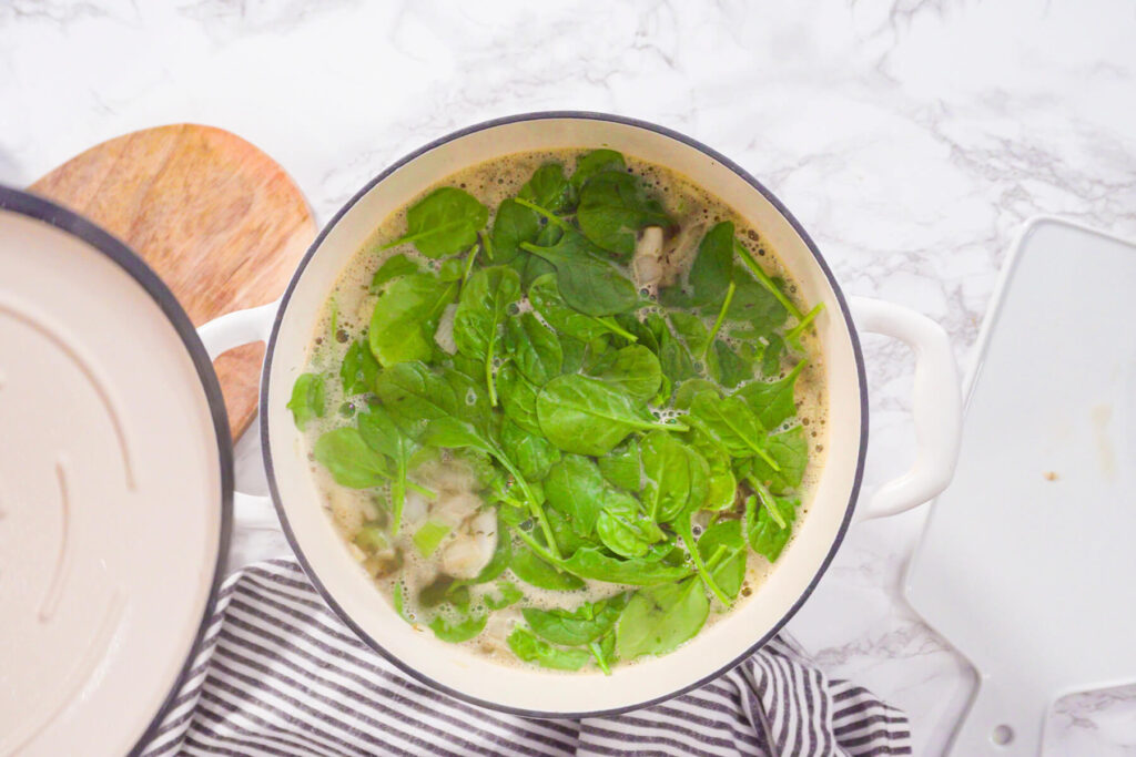 Frischer Babyspinat liegt auf der heißen Bohnensuppe im Topf, bevor er untergehoben wird