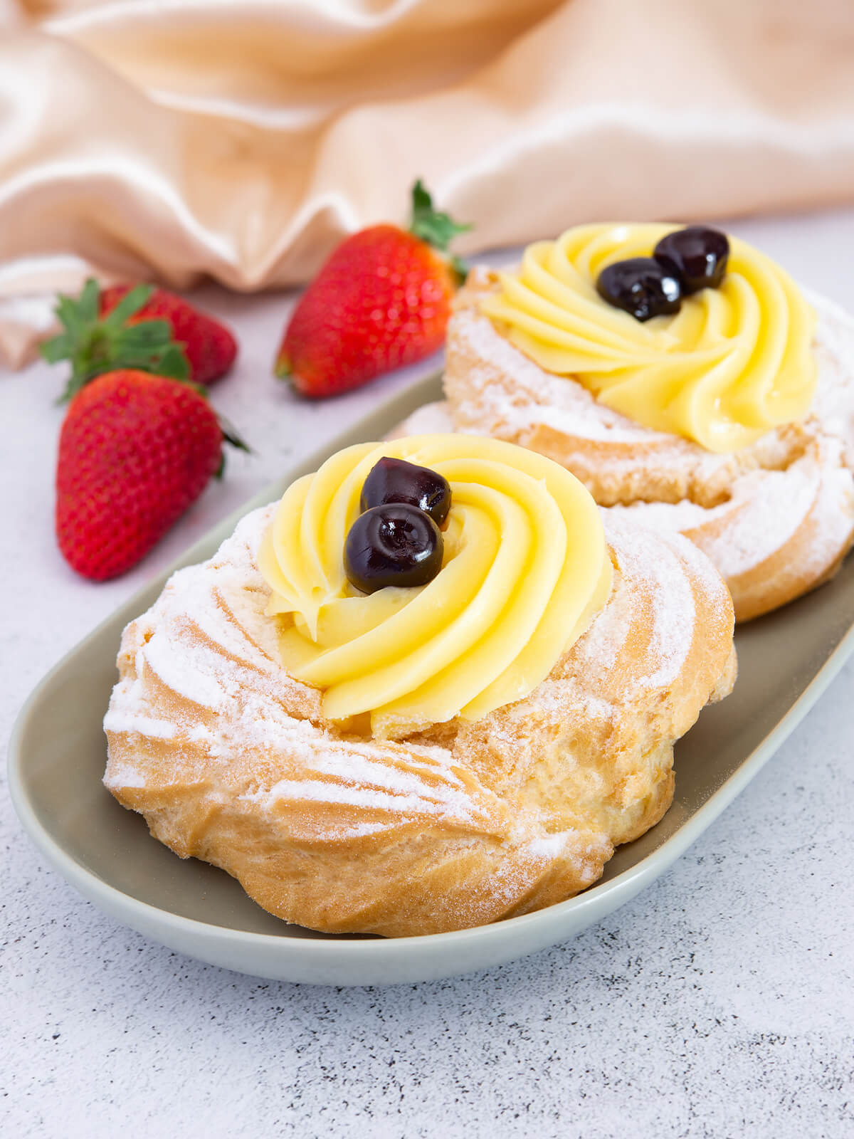Zwei gefuellte Zeppole di San Giuseppe auf einer ovalen Servierplatte