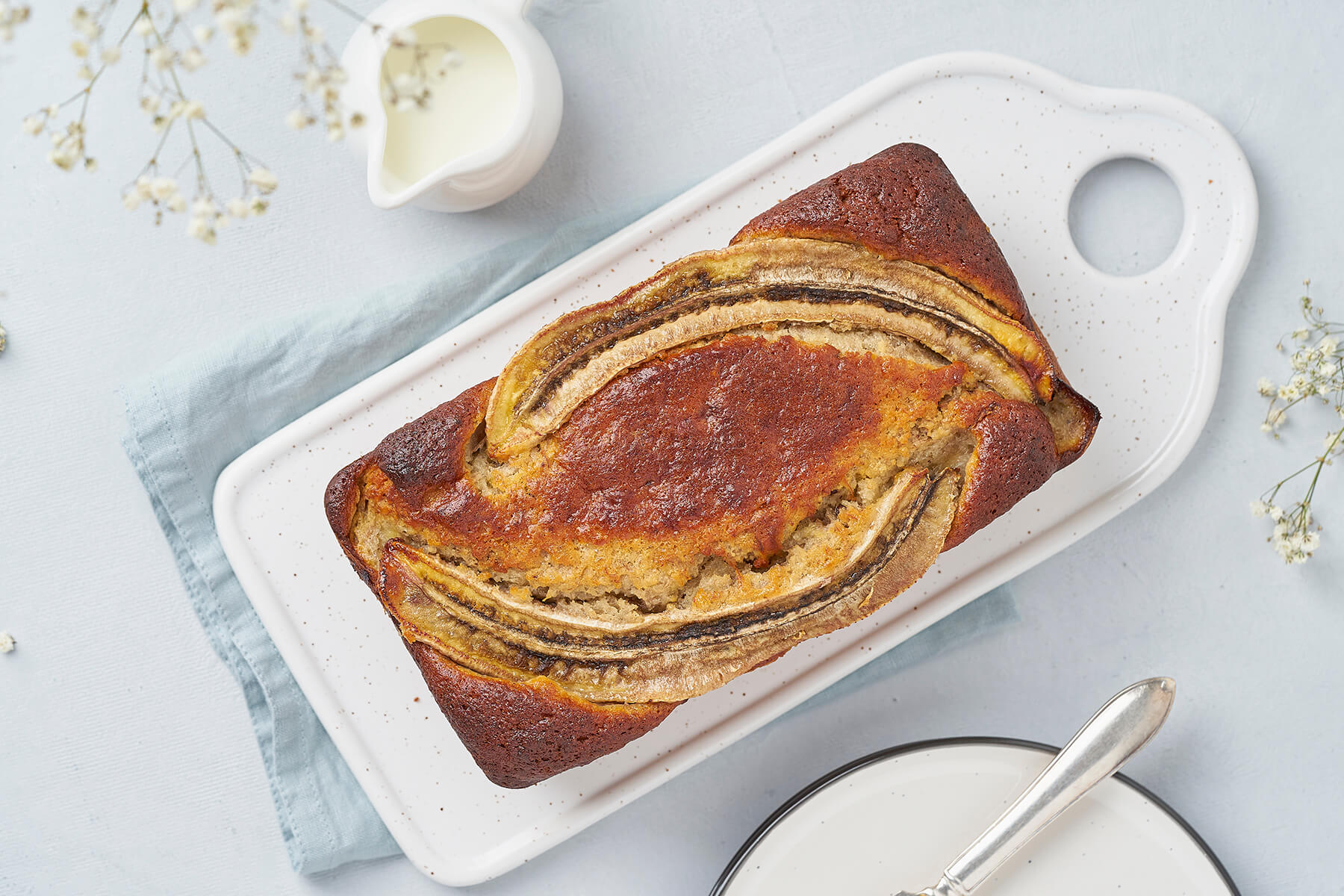 Ganzes Bananenbrot mit Walnüssen und Schokolade von oben, drei karamellisierte Bananenhälften rahmen die dunkel gebackene Mitte
