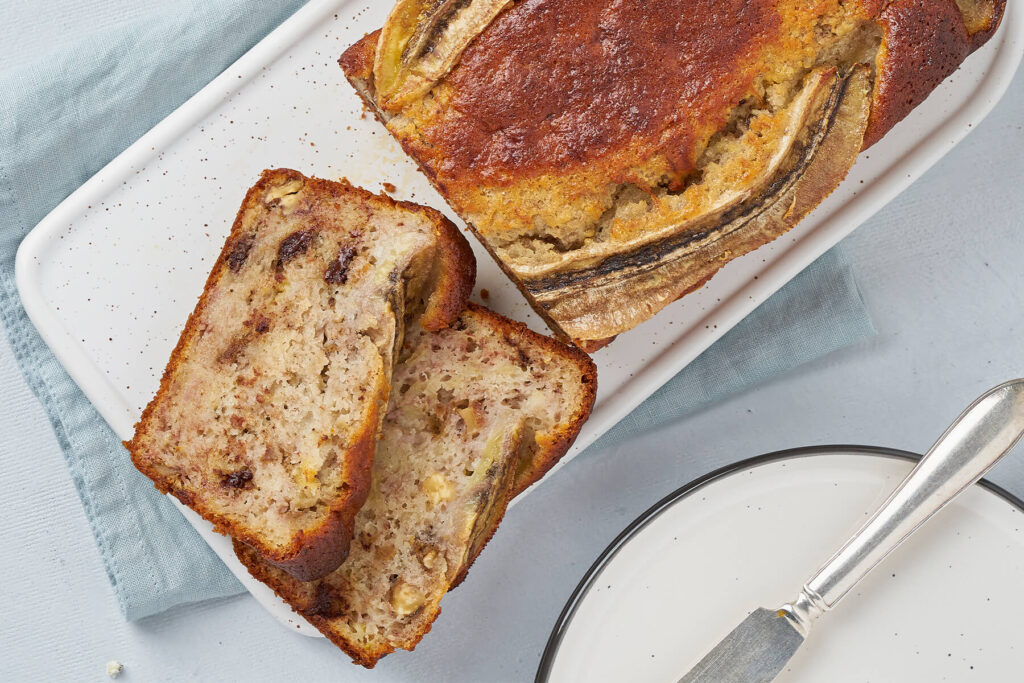 Aufgeschnittenes Bananenbrot mit Walnüssen und Schokolade von oben, zwei Scheiben liegen neben dem Laib