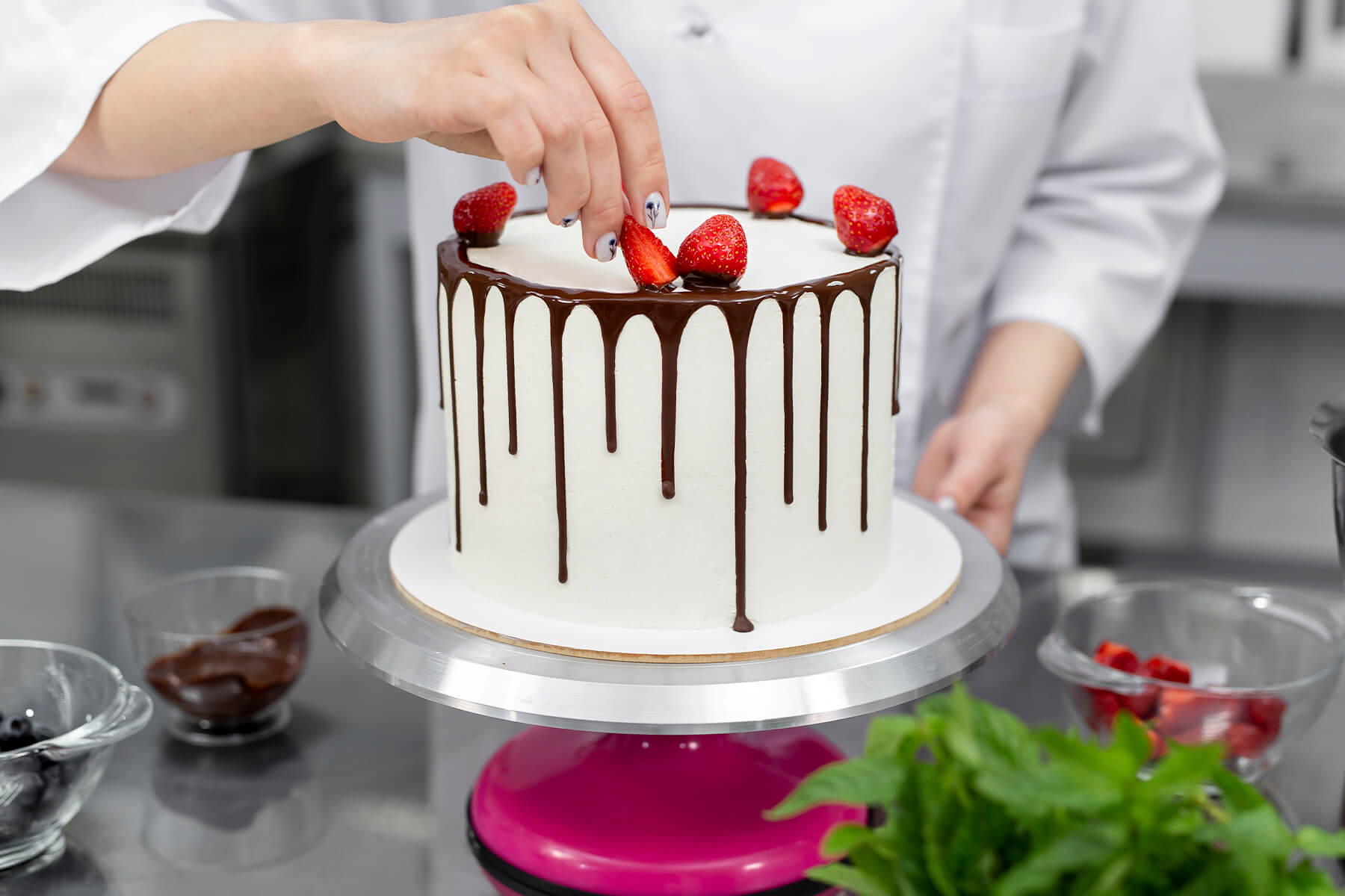 Erste Erdbeeren werden auf den noch glänzenden, weichen Schokoladenrand einer weißen Torte gesetzt