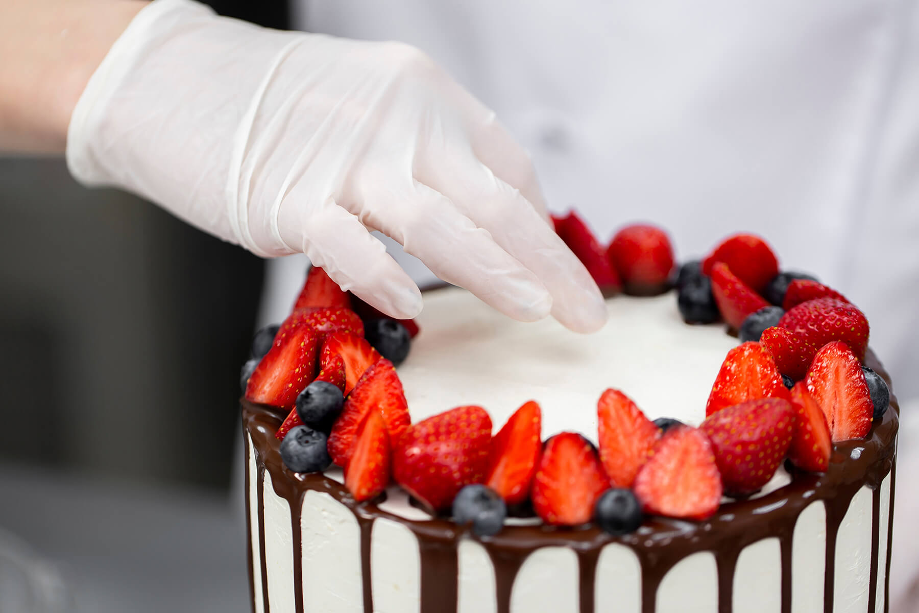 Nahaufnahme des geschlossenen Kranzes aus halbierten Erdbeeren und Heidelbeeren auf dem dunklen Schokoladenrand