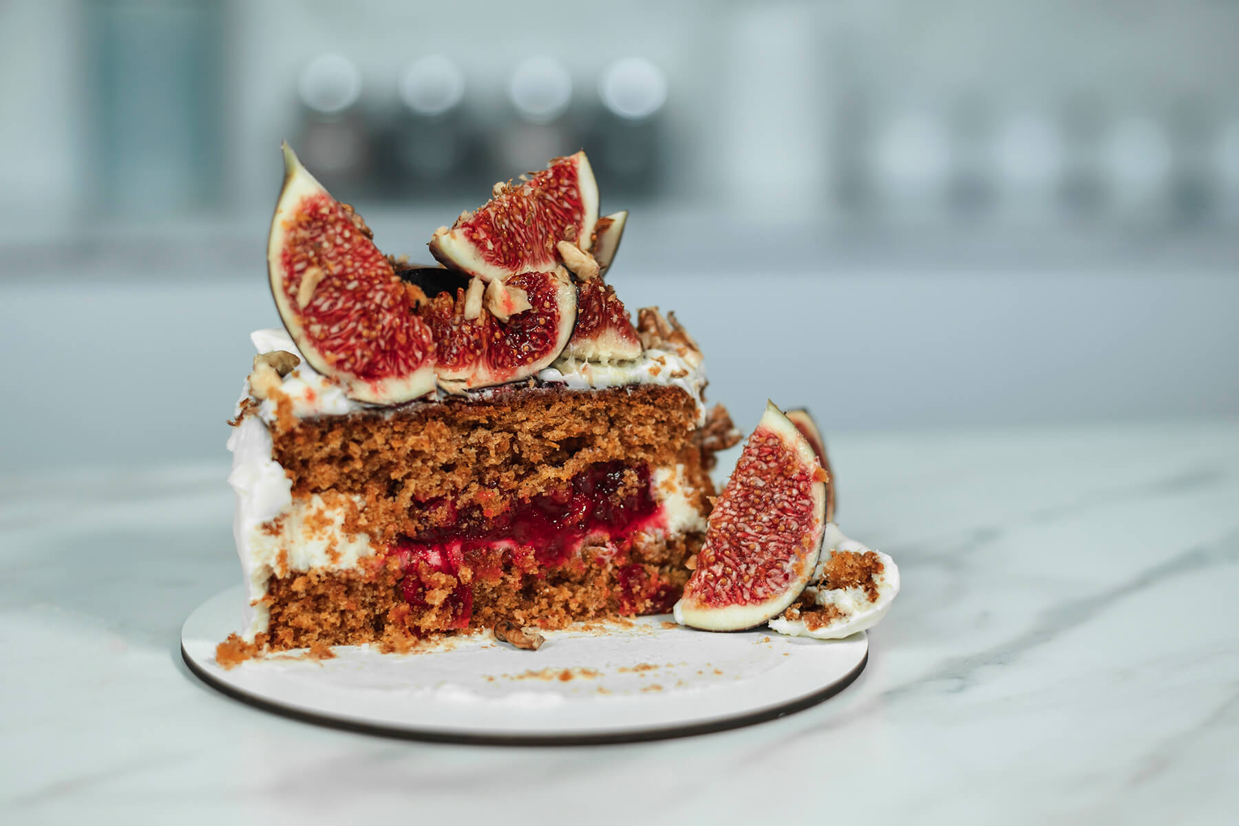 Tortenstück im Anschnitt mit zwei Möhrenkuchenböden, weißer Creme, roter Beerenfüllung zwischen den Böden, obenauf Feigenviertel und gehackte Walnüsse