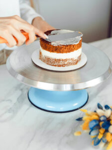 Winkelpalette verteilt eine dünne, halbtransparente Cremeschicht auf der Oberseite einer zweistöckigen Torte, der Kuchen schimmert darunter durch