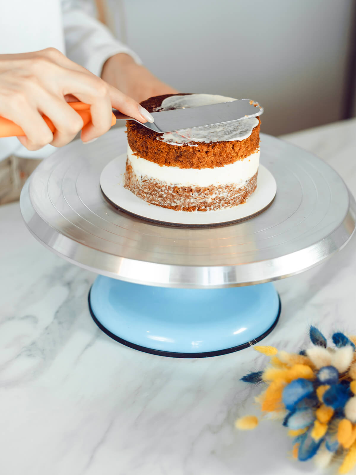 Winkelpalette verteilt eine dünne, halbtransparente Cremeschicht auf der Oberseite einer zweistöckigen Torte, der Kuchen schimmert darunter durch