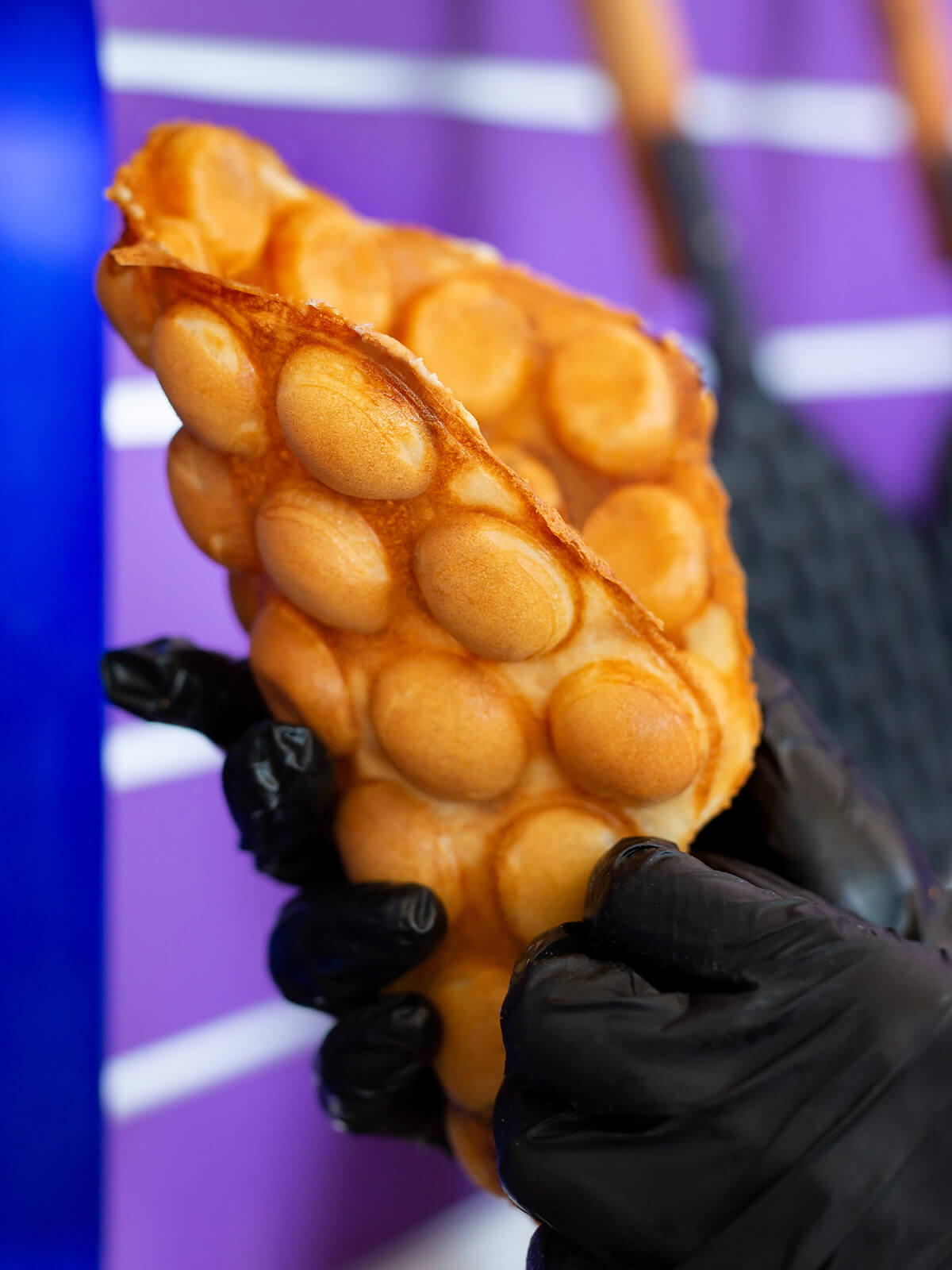 Zur Tüte gefaltete Bubble Waffle in der Hand, außen die runden Blasen, an der Bruchkante die glatte dünne Rückseite