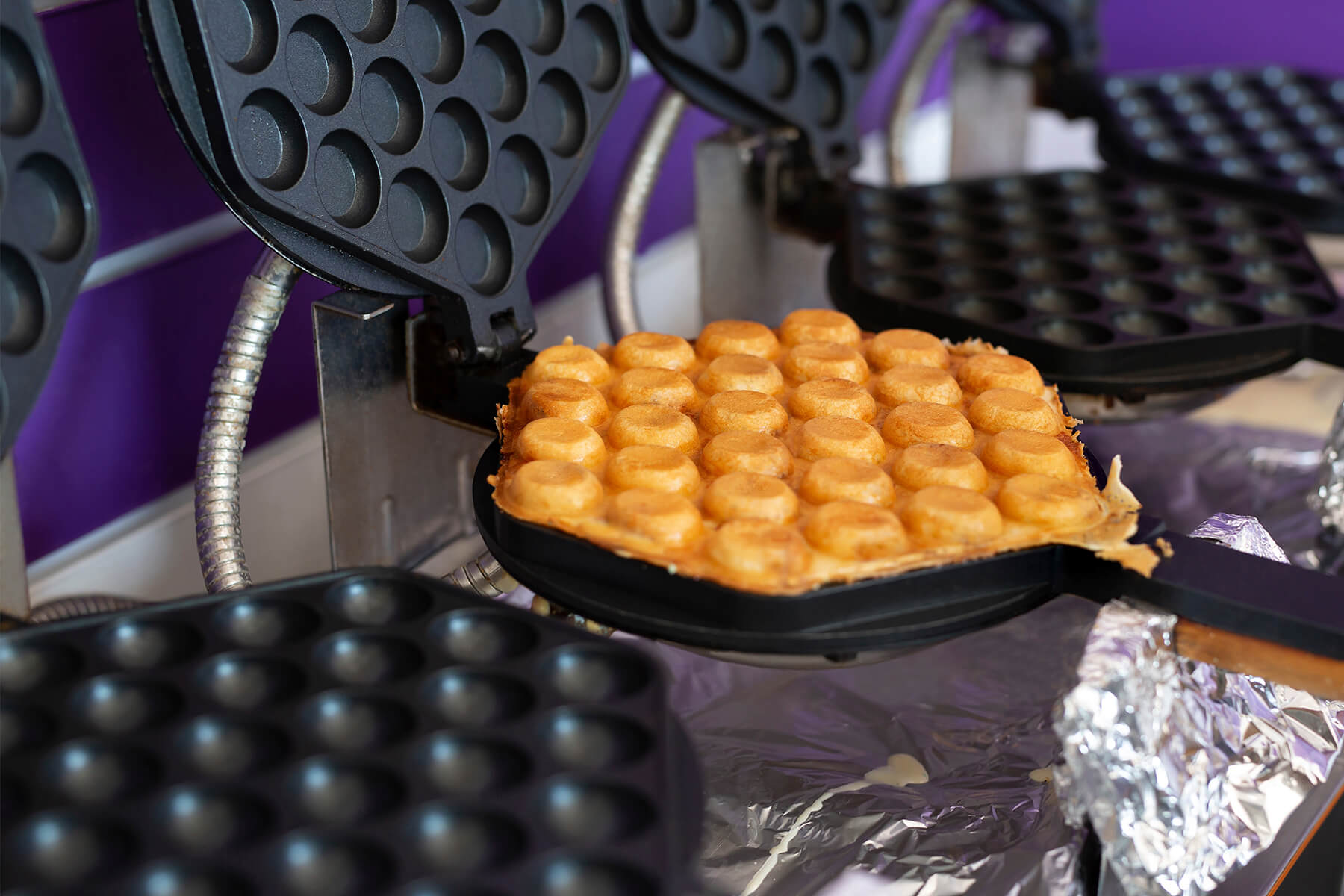 Geöffnetes Bubble-Waffle-Eisen mit der fertig gebackenen goldenen Waffel, ringsum die tiefen halbrunden Mulden der Platten