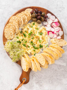 Fertiges Butter Board von oben mit Crackern, Oliven, Radieschen, Sprossen und Baguettescheiben rundherum