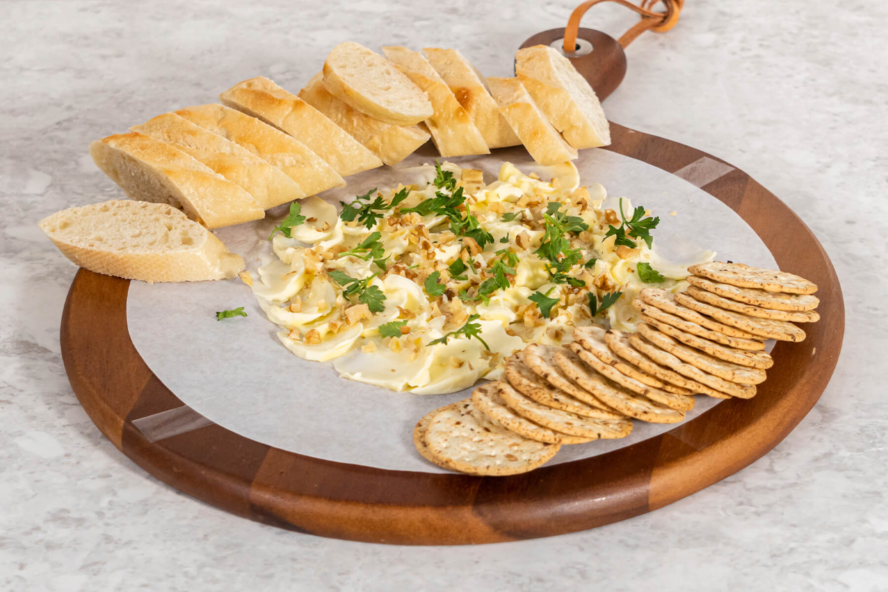 Butter Board auf rundem Holzbrett mit Baguettescheiben und runden Crackern zum Servieren