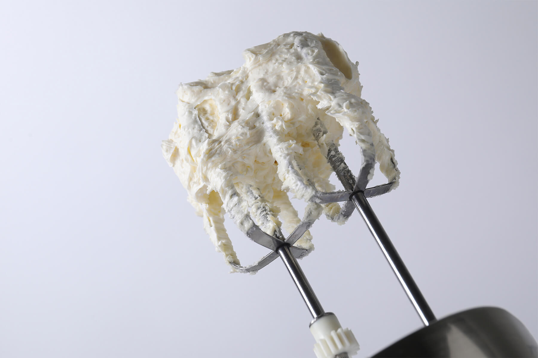 Feste Buttercreme sitzt oberhalb der Quirle eines Handmixers und hängt in dicken Strängen zwischen den Streben