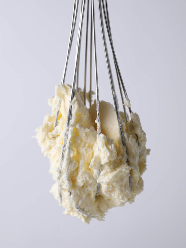 Großer Klumpen fertig aufgeschlagene Buttercreme hängt kopfüber am Schneebesen und fällt nicht ab