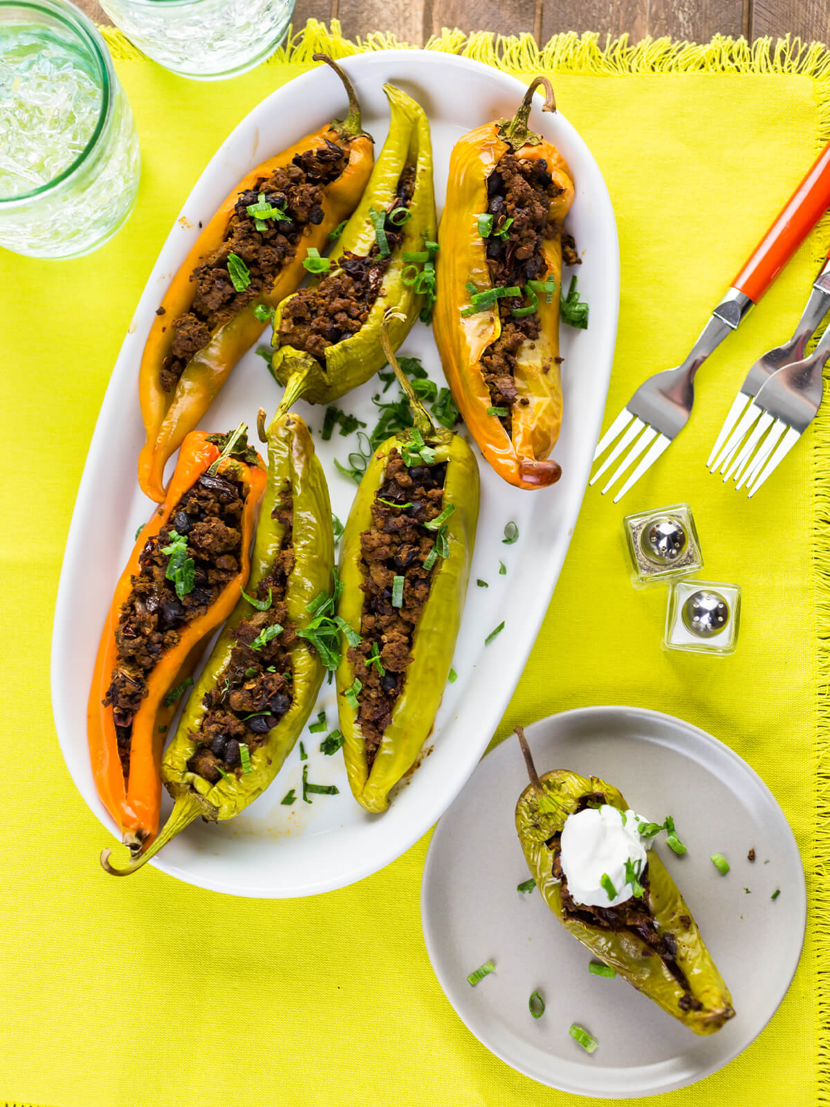 Gefüllte Chilischoten in Grün, Gelb und Orange nebeneinander auf einer weißen ovalen Platte, von oben fotografiert, mit Frühlingszwiebelringen bestreut