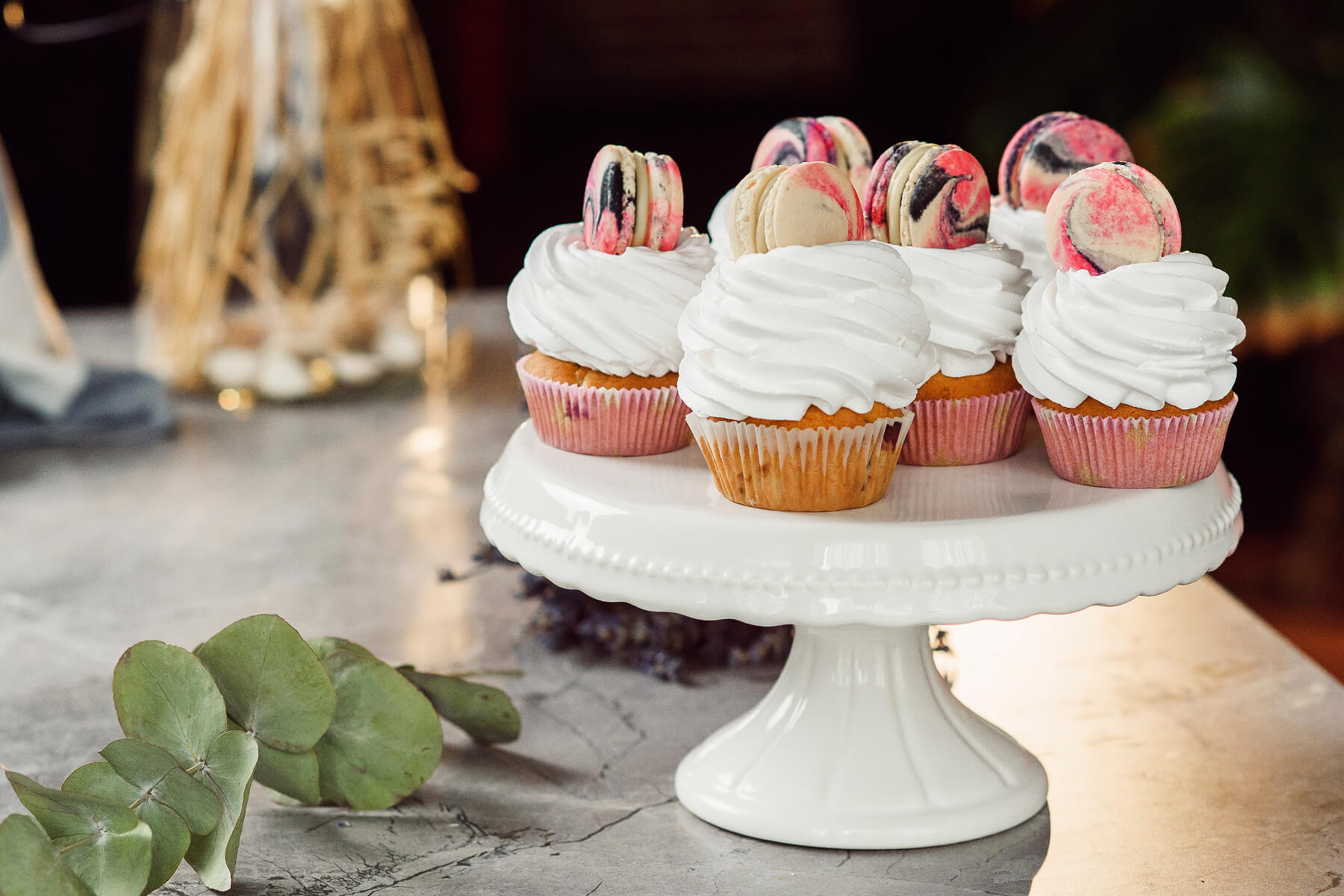 Sechs Gebäckstücke mit weißen Cremehauben und marmorierten Macarons auf einer weißen Porzellanplatte