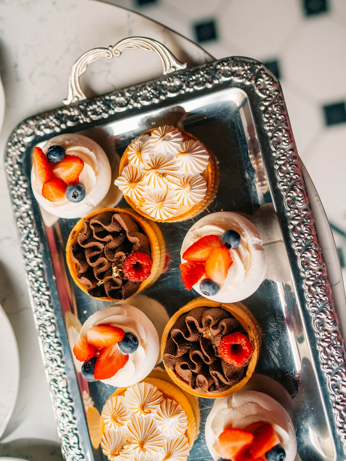 Silbertablett von oben mit Baiserschalen mit Sahne und Beeren neben Tartelettes mit Baiserhaube und Schokoladencreme