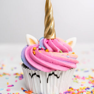 Einhorn-Cupcake mit rosa-blauer Regenbogenhaube, goldenem Horn, weißen Fondant-Ohren und aufgemalten Augen auf dem Papierförmchen