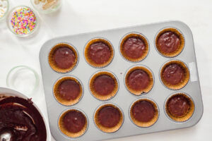 Muffinblech mit zwölf zu zwei Dritteln gefüllten Papierförmchen voll dunklem Schokoladenteig